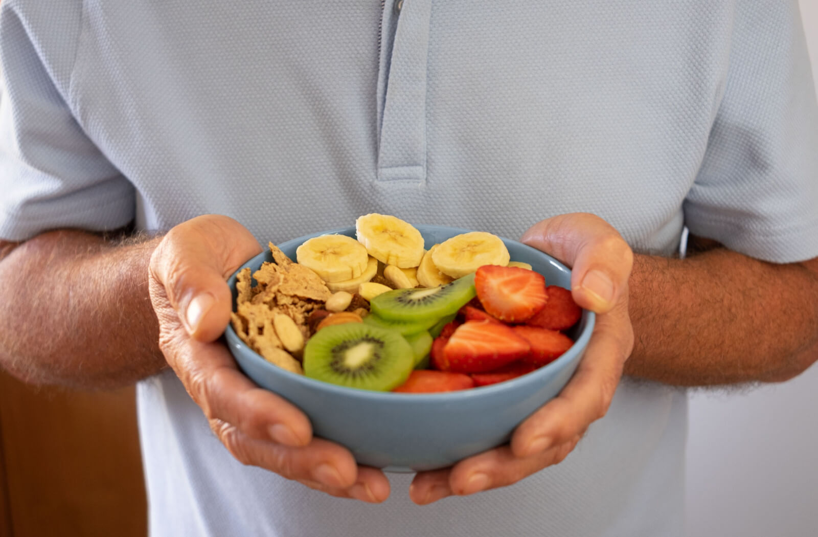 A Senior man holding plate of fruits and nuts.