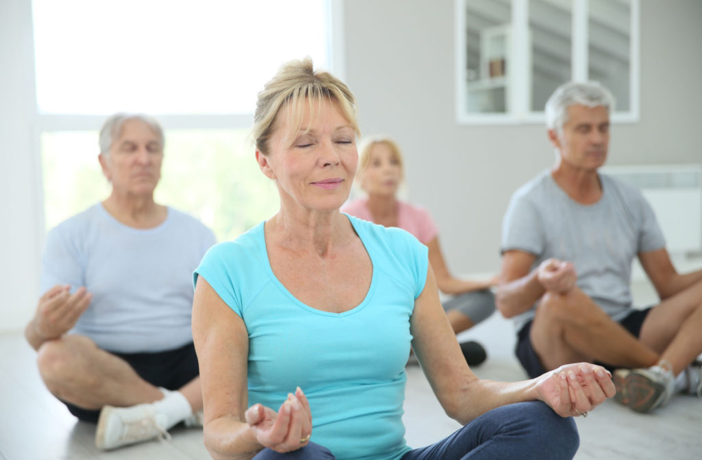 A group of older adults with eyes close doing yoga.