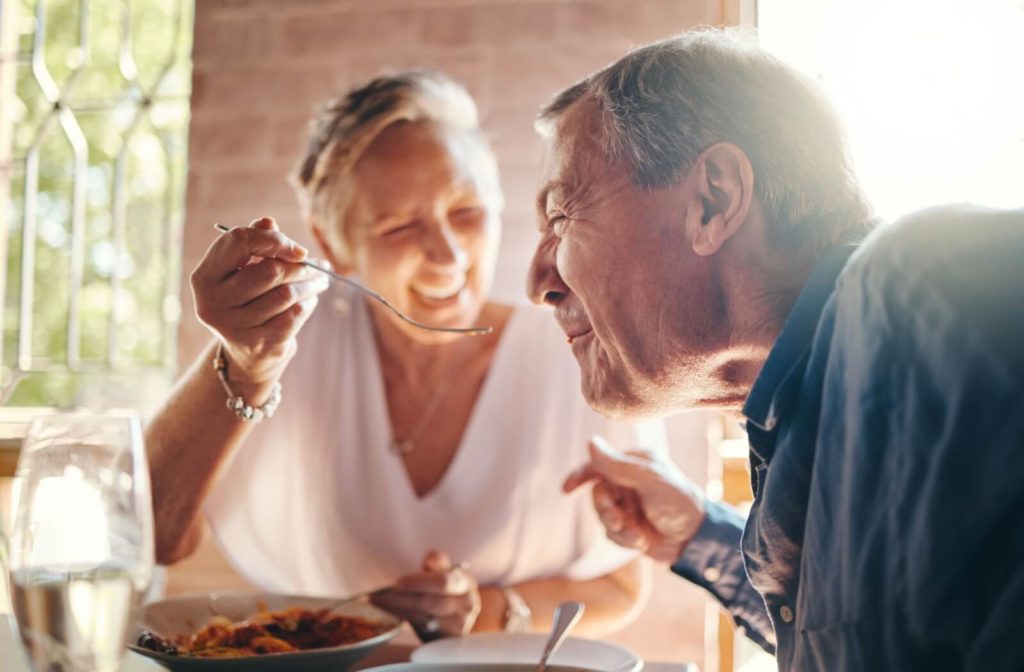 A senior couple laugh together as one feeds the other a bite of food as a way of enjoying eating more