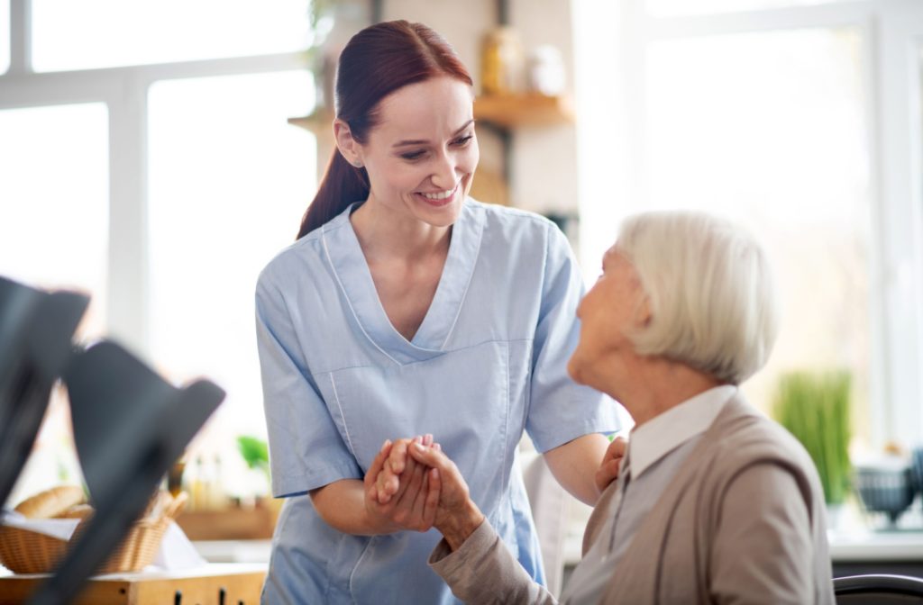 A caregiver smiling at an older adult and holding their hand in assisted living.