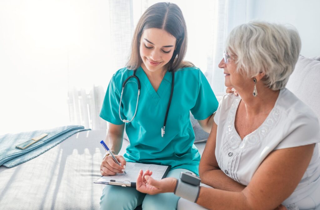 A caregiver in assisted living recording a resident's blood pressure and smiling during a healthcare checkup.