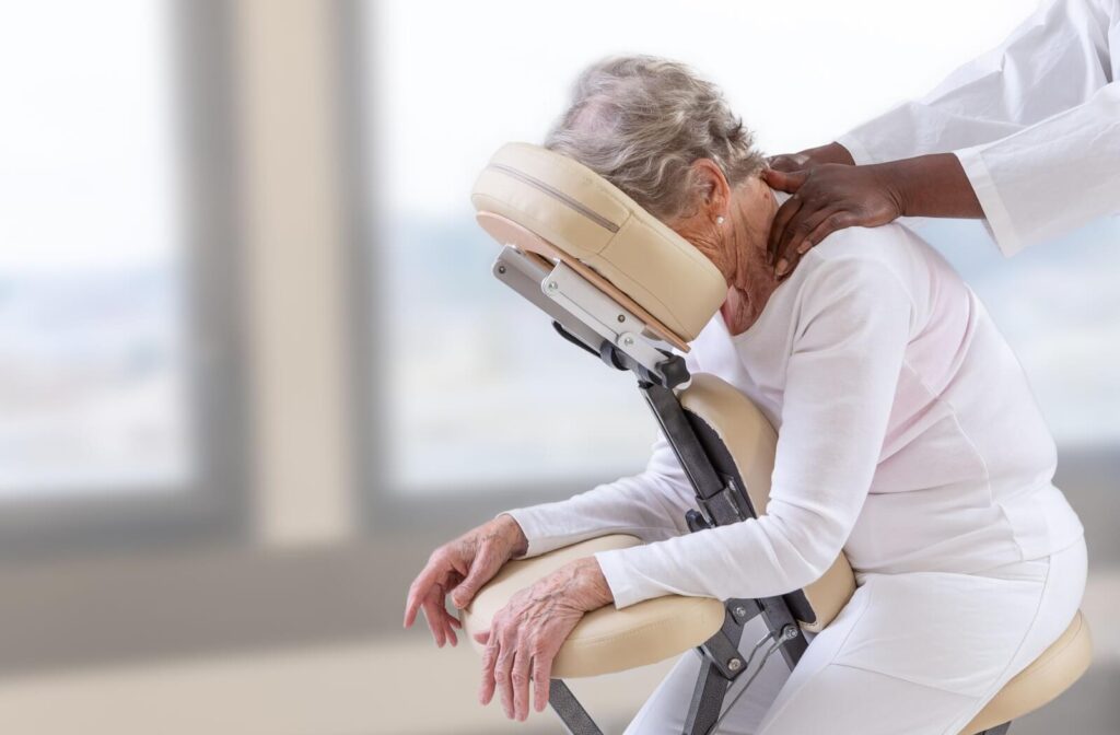 An older adult sits in a massage chair, receiving an upright massage to alleviate chronic pain.