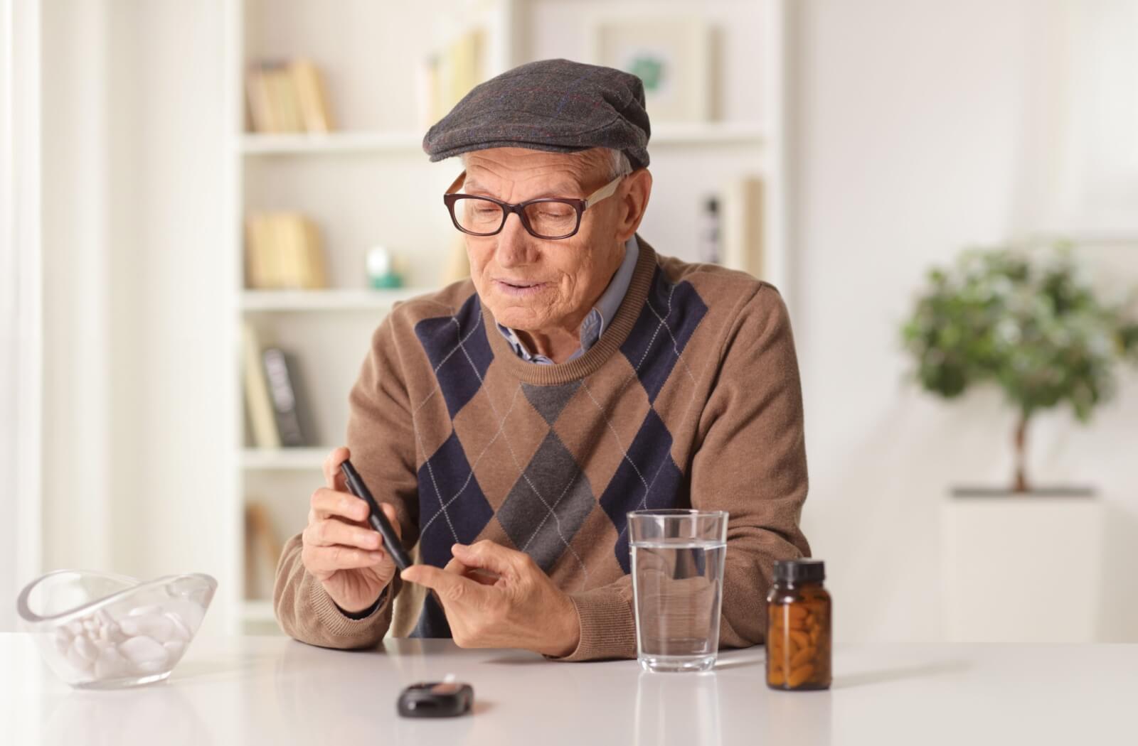 A senior sitting at a table with their morning medication and a glass of water checks their blood sugar levels