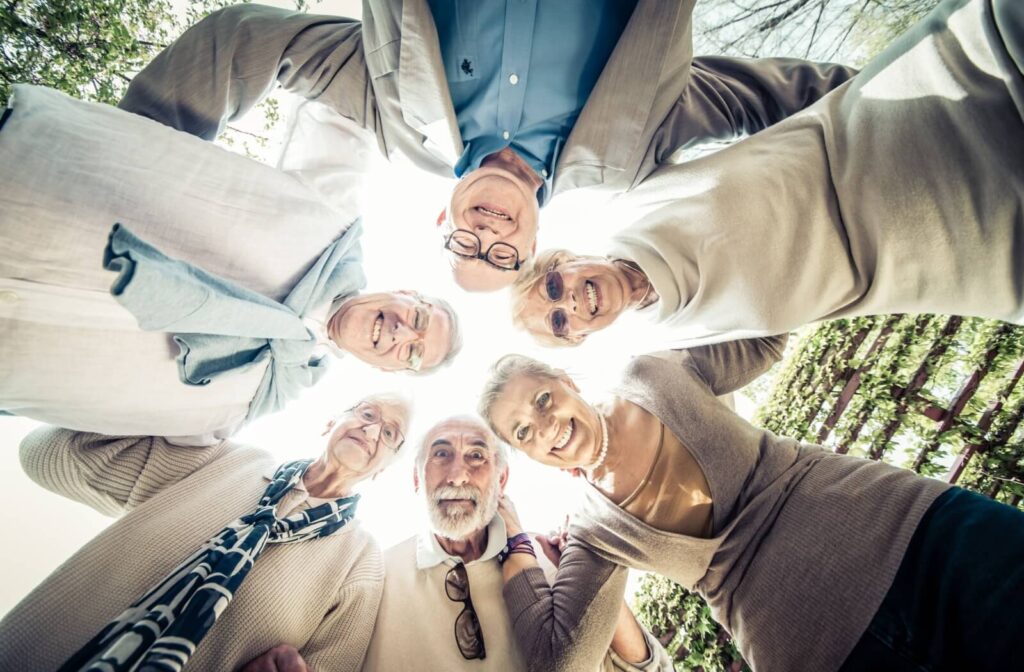 A group of seniors friends gather together in a circle, smiling for a picture while socializing outdoors