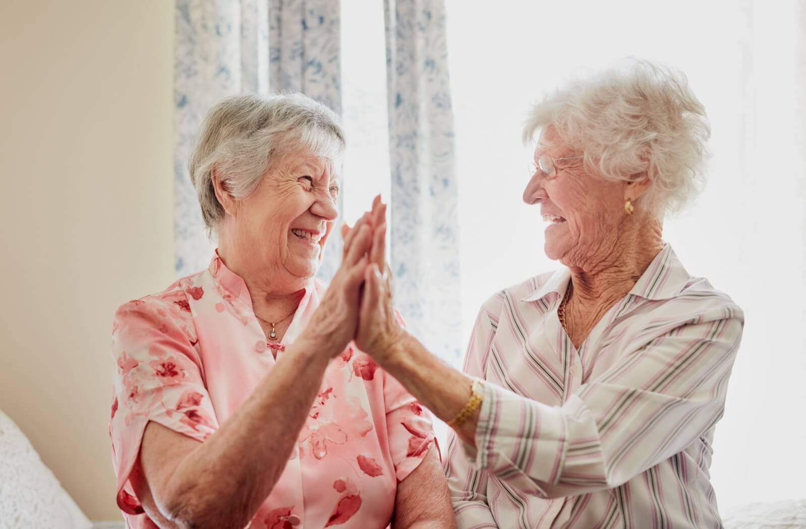 Two seniors in senior living give each other a high-five, laughing and enjoying each other’s friendship and company