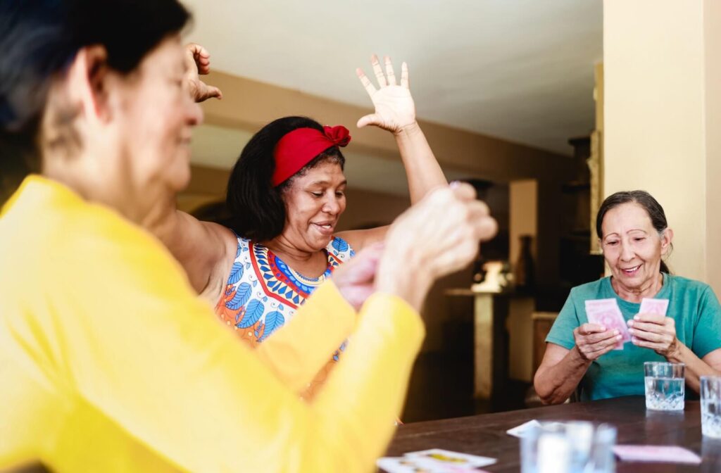 Three seniors laugh and celebrate together while playing cards and enjoying each other’s company