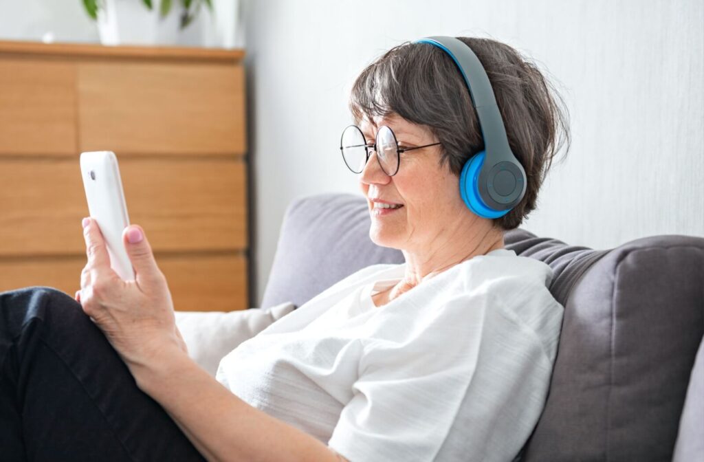 A senior uses headphones to listen to an audiobook, following along with an electronic version of the book on their phone