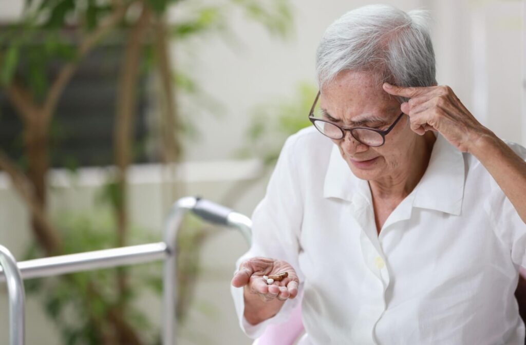 A senior holding a handful of pills furrows their brow in confusion, trying to remember whether they’ve taken them already